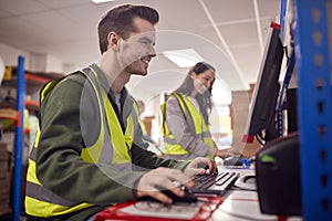 Staff In Busy Modern Warehouse Working On Computer Terminals