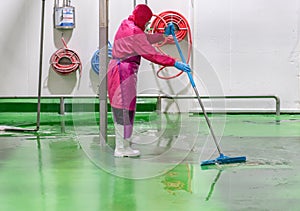 Staff hygien cleaner in protective uniform cleaning floor of food processing plant