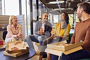 Staff At Informal Meeting In Office With Takeaway Pizza And Drinks