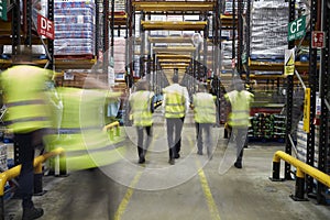 Staff in reflective vests walking in a warehouse, back view