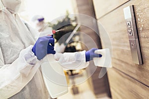 Staff using disinfectant from the bottle spraying an elevator push button control panel.