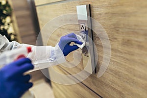 Staff using disinfectant from the bottle spraying an elevator push button control panel.