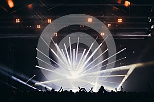 Stage lights and crowd of audience with hands raised at a music festival. Fans enjoying the party vibes