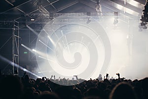 Stage lights and crowd of audience with hands raised at a music festival. Fans enjoying the party vibes