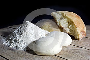 Stages of Making Bread-Flour, Dough and Loaf of Bread on Wooden Table Over Black Background