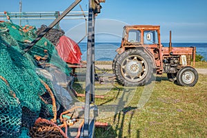 Stagnating, dull business in the fishing industry: illustration with an old farm tractor and unused fishing nets by the sea