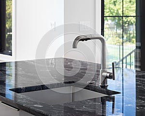 A stainless kitchen faucet detail on a black marble countertop.