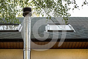 Stainless steel chimney flue on the tile covered roof with windows at country cottage