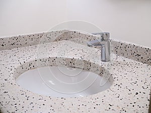 Stainless steel chrome silver tap or faucet in round shape of terrazzo tiles wash basin on white wall background.