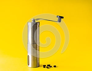 Stainless steel coffee grinder by handle Equipment for making coffee at home And roasted coffee beans On bright yellow, background