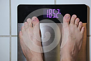 Stainless steel digital scale with mans feet weighing 185 pounds on tile floor