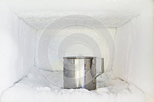 Stainless steel drinking water glass in freezer of a refrigerator. Ice buildup inside of a freezer walls.