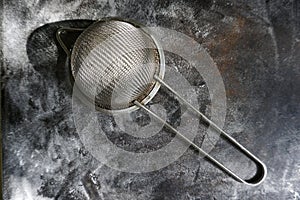 Stainless Steel Fine Mesh Strainer Colander Flour Sieve with Handle on dark background powdered with flour. Kitchenware