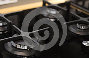 Stainless steel gas hob detail on black stone worktop, close-up, matte black stylish four burner