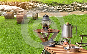 Stainless steel kettle, portable gas stove and vintage lanterns on wooden picnic table set near the stream in natural view