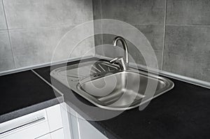 Stainless steel kitchen sink on a dark grey granite worktop. Kitchen sink and water tap in the kitchen.