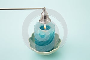 Stainless steel put out candle flame wick long handle candle snuffer bell with lit blue candle on blue studio background.