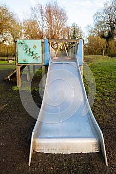 Stainless steel silver slide coming off wooden play structure in children's playground.