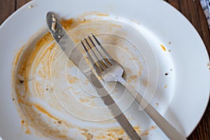 Stainless steel simple knife and fork on a dirty white plate with napkin after diner on a wooden table surface