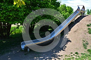 Stainless steel slide on a playground with grassy hills. playground with stone walkways made of natural sandstone stone. a pipelin