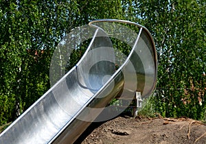 Stainless steel slide on a playground with grassy hills. playground with stone walkways made of natural sandstone stone. a pipelin