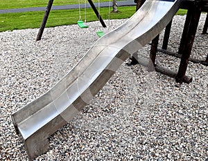 Stainless steel slide and swings on the playground in the park in gray pebbles
