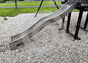 stainless steel slide and swings on the playground in the park in gray pebbles