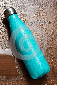 Stainless steel thermos bottle isolated on a wooden table sprayed with water. Light blue color.