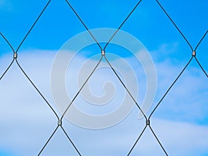 Abstract view of stainless steel mesh fence with clamps and blue sky background