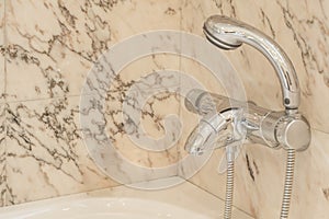 Stainless steel water temperature and flow taps in the corner of a marble walled bathroom