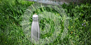 Stainless thermo bottle in green grass.