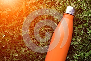 Stainless thermos water bottle, matte orangecolor. Mockup isolated on green grass background with sunlight effect.