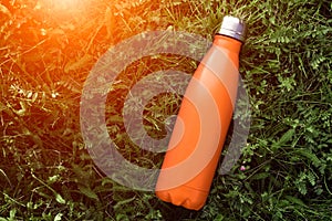 Stainless thermos water bottle, matte orangecolor. Mockup isolated on green grass background with sunlight effect.