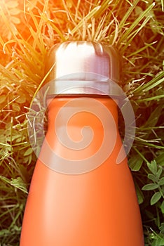 Stainless thermos water bottle, orange color. Mockup isolated on green grass background with sunlight effect. Glossy aluminum vacu