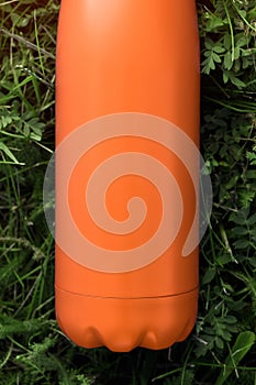 Stainless thermos water bottle, orange color. Mockup isolated on green grass background with sunlight effect. Glossy aluminum vacu