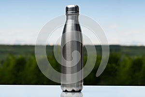 Stainless thermos, water bottle on the sky and forest background.