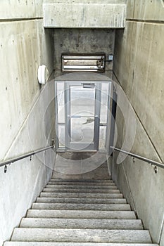 Staircase inside a building going down to a glass door that leads to outdoors