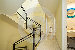 Staircase interior of detached house with cream marble floors, metal and glass railing and pale yellow walls