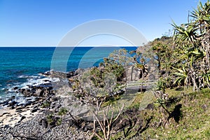 Staircase leading down to rock and sand filled beach with beautiful blue ocean