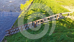 A staircase with a railing made of wood leads from the river bank along a slope overgrown with grass to the lawn. The river has fa