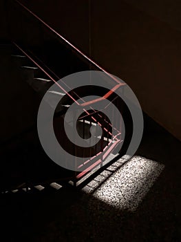 Staircase with a red metal handrail and  trace of light in the dark