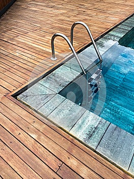 Staircase in the rimless pool of a spa, with the exterior surrounded by teak wood, deep blue crystal clear water