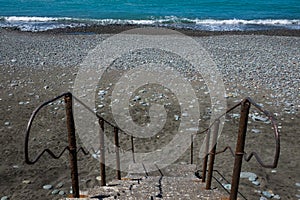 Staircase to beach. Blue water and stones on beach