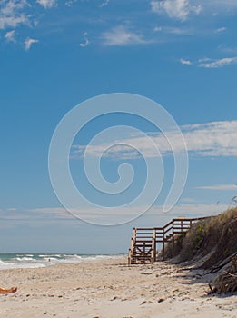 Stairs on a beach in central Florida with sunbather and people swimming. Serene beach scene with blue sky, sand and waves photo