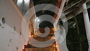 Stairs of Buddhist temple lit with rows of oil lamps, celebrating Vesak. Devotees climb to worship, evening ambiance