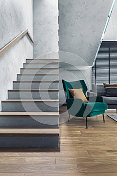 Stairs in modern living room interior. Green velvet armchair and minimalist personal accessories. Concrete walls. Home decor.