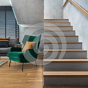 Stairs in modern living room interior. Green velvet armchair and minimalist personal accessories. Concrete walls. Home decor.