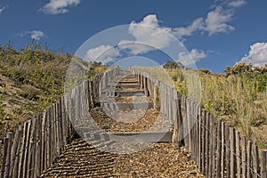 Stairs uphill in the dunes under a blue sky with fluffy clouds