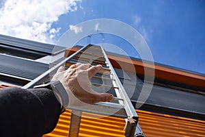 Stairway to Heaven. A man reaches out with his hand for a metal staircase in a building against the background of the sky and