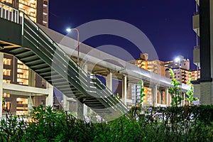 Stairway to pedestrian overpass and elevated train track through city at night